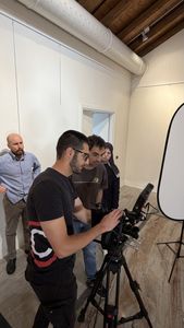 THRIVE Academy participants learn to operate a professional video camera during a hands-on digitalisation workshop, with a large reflector positioned beside the filming area.