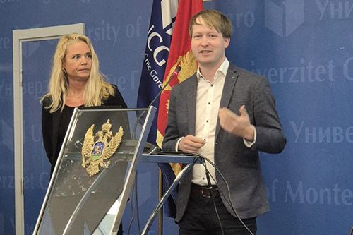 A man in a grey blazer speaking at a podium next to a colleague during a formal event at the University of Montenegro.